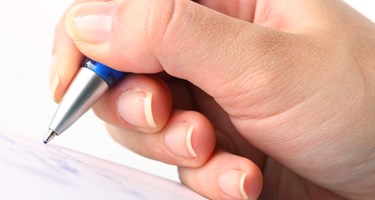 Photograph showing a hand holding a pen about to start writing on paper